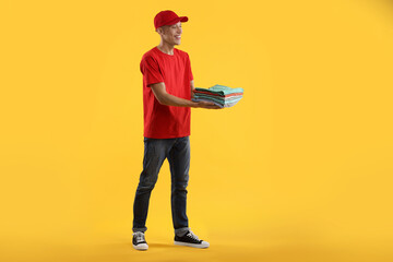 Dry-cleaning delivery. Happy courier holding folded clothes on orange background