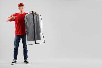 Dry-cleaning delivery. Happy courier holding garment cover with clothes on light grey background,...
