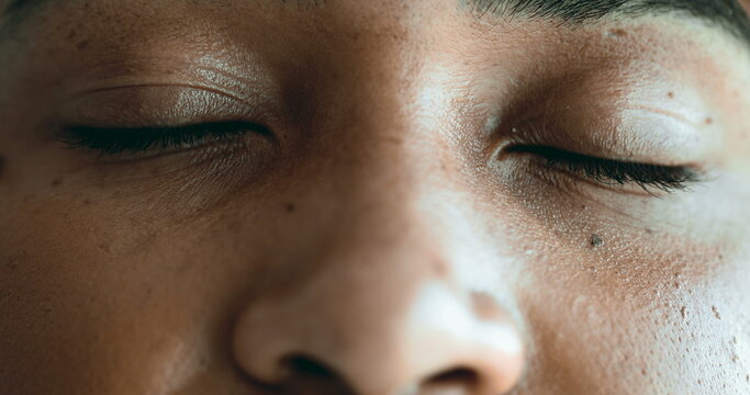 One meditative young black woman closing eyes in relaxation and contemplation. Macro close-up detail of facial features in quiet rest, opens eye smiling at camera