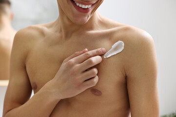 Man applying moisturizing cream onto his shoulder indoors, closeup