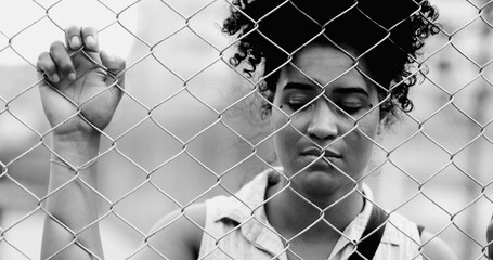 One trapped young black woman leaning on urban metal fence in monochromatic portrait struggling...
