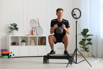 Smiling sports blogger training with kettlebell while streaming online fitness lesson at home