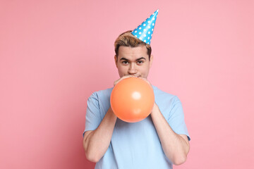 Young man with party hat and balloon on pink background