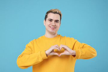 Naklejka premium Young man showing heart gesture with hands on light blue background