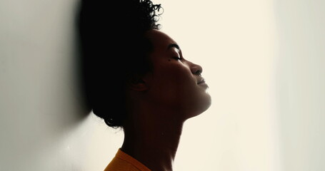 One pensive young black woman with eyes closed leans on wall with thoughtful contemplative...