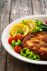 Crispy breaded fried pork chop, green asparagus and fresh vegetables on wooden table
