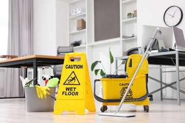 Cleaning service. Mop, wet floor sign and bucket with supplies in office