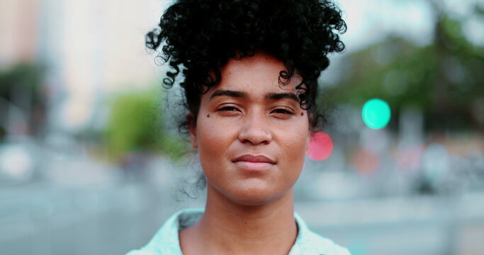 One young black Latina woman staring at camera with serious solemn expression. Portrait of 20s person of African descent in urban setting in background