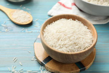 Raw basmati rice in bowl on light blue wooden table, closeup. Space for text