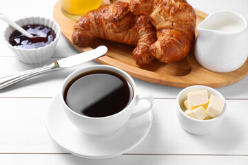 Fresh croissants, butter, jam and coffee on white wooden table. Tasty breakfast