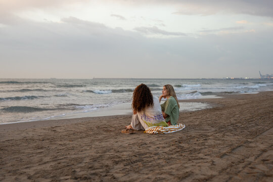 Relaxed women sitting at beach in front of sea and talking