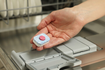 Woman putting detergent tablet into open dishwasher, closeup