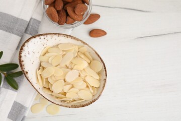 Fresh almond flakes and nuts on white wooden table, flat lay. Space for text