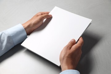 Man holding blank notebook at light grey table, closeup. Mockup for design