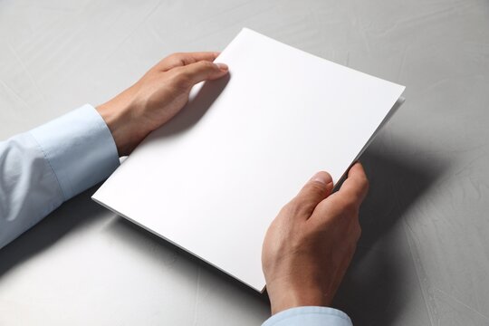 Man holding blank notebook at light grey table, closeup. Mockup for design