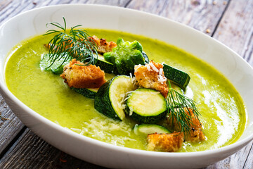 Cream zucchini soup with croutons, Parmesan cheese and fresh dill on wooden table
