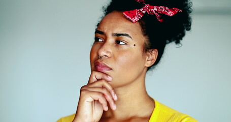 Thoughtful Young African American woman pondering solution to problem putting hand in chin in deep...