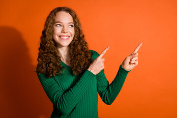Photo of cheerful dreamy lady dressed green shirt looking pointing two fingers emtpy space isolated orange color background