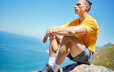 Man, hiking and rest on mountain by sea, ideas and vision with reflection with blue sky in summer. Person, relax and memory with peace on rocks by ocean, thinking and nature for trekking adventure