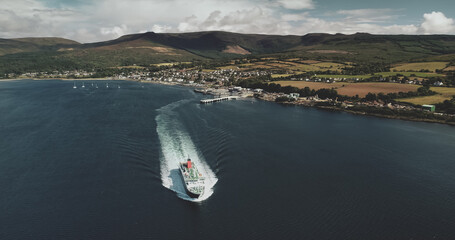 Scotland's ocean, passenger ferry aerial view in coastal water of Firth-of-Clyde Gulf. Ship crossing from Brodick terminal to Scottish mainland. Cityscape at green valleys.