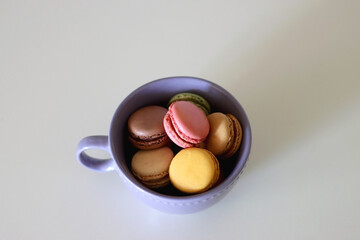 Purple cup filled with pastel macarons on white background. Selective focus.