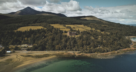 Scotland's ocean coast landscape aerial view: forests, valleys, hills. Brodick castle - historical ancient building in Arran Island. Road with riding cars shot