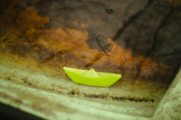 Origami paper green boat inside bigger wooden boat with water 