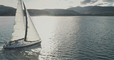 Sun shine over yacht at mountain island coast aerial. Luxury sailboat regatta at sea gulf. Sunlight...