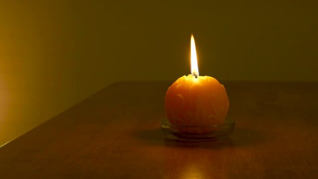 Yellow round wax candle with flickering yellow flame in a dark room