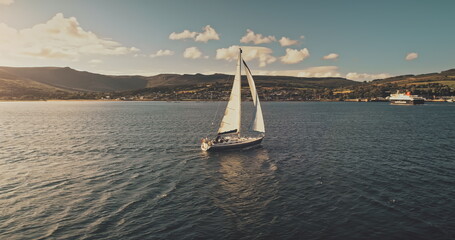 Sailboats at ocean coast aerial. Summer cruise on luxury passenger yacht. Scotland sea shore of green mountains Arran island. Water transport at amazing sea at cinematic drone shot