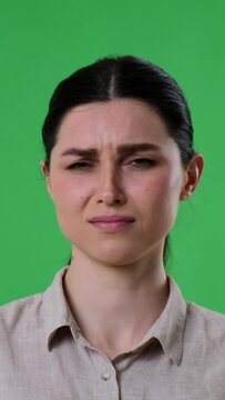 Unhappy Caucasian woman negative reacted to smelly odor on green background. Disgust, displeasure, discontent content. Vertical video.