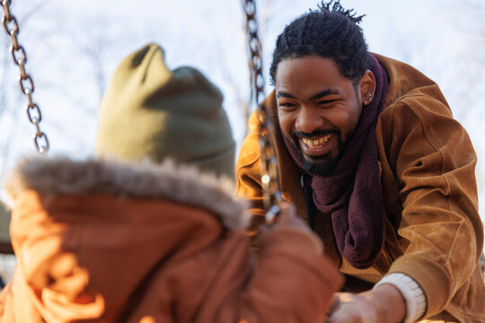 Father having fun with boy playing on swing in park