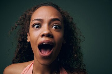 Face, surprise or alarm with crazy woman, funny or comic with wide eyes on green background. Wild,...