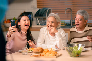 Family Togetherness in the Kitchen: Asian Mother Prepares a Happy Dinner, Joined by Father, Daughter, and Senior Elderly, Creating Fun and Memorable Meals, A Heartwarming Holiday Gathering - obrazy, fototapety, plakaty