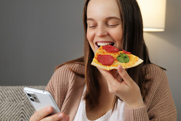 Optimistic positive pretty young Caucasian woman indoors at home eating pizza chatting by phone...