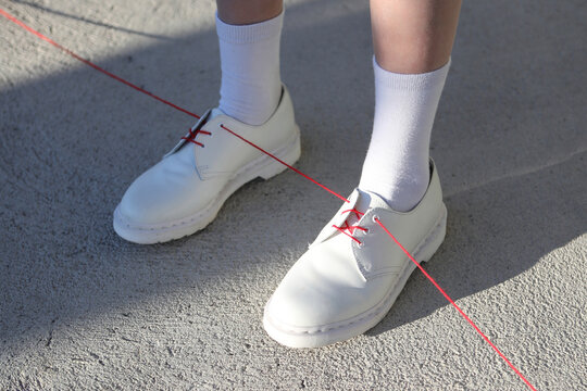 White shoes with one red lace/ribbon. Illustration of red thread 