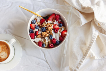 Breakfast bowl with granola and berries standing on the bed, view from the top
