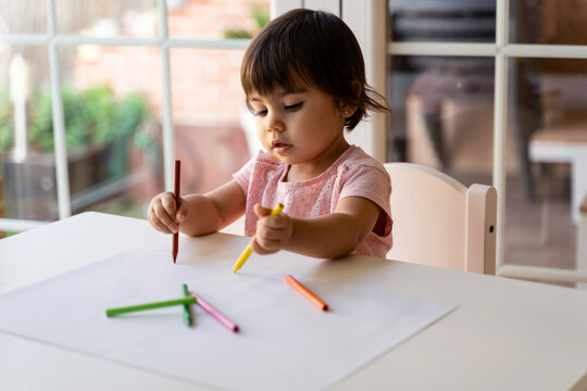 girl drawing with colored pencils at table in living room