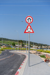 An urban area entrance sign coupled with a roundabout warning, under the clear spring sky of Israel.