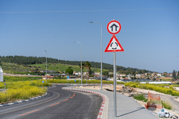 Pair of road signs against a blue sky, with the first indicating an upcoming roundabout and the...