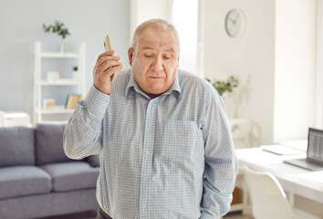 Elderly man looks puzzled as he talking on the mobile phone call at home. Engaged in a phone...