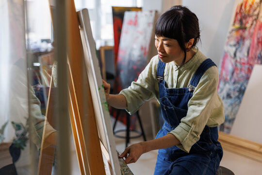 Asian female artist painting on canvas in art studio 