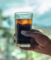 Close-up of a hand holding a glass of fresh cola drink, with ice. Beautiful light in the bubbles. Bright background.