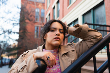 Fashionable woman leaning on a railing in a vibrant street.