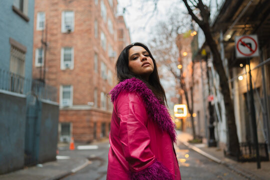 Confident woman in a pink coat standing in an alley. 