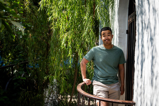 Silly smile from a gen z guy standing on a balcony next to a fern