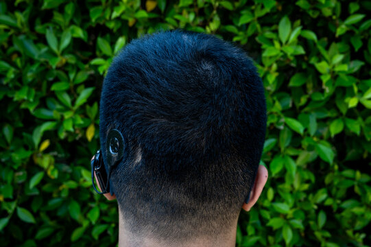 A guy with a cochlear implant in front of a tropical green leaf wall