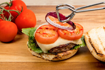 A cheeseburger with Havarti cheese tomatoes and red onions and lettuce on a toasted cornmeal bun on...
