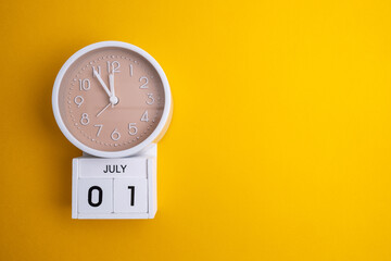 July 1st. Wooden calendar with the date July 1 and a clock on a colored background with copy space. First summer day. Empty space for text