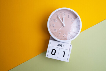 July 1st. Wooden calendar with the date July 1 and a clock on a colored background with copy space. First summer day. Empty space for text